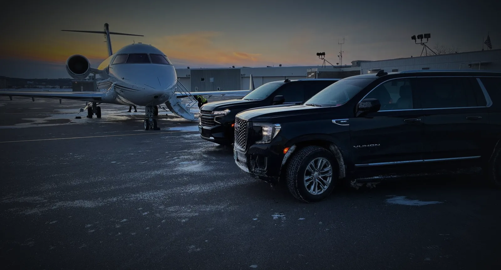 Black SUVs staged beside a private jet at sunrise