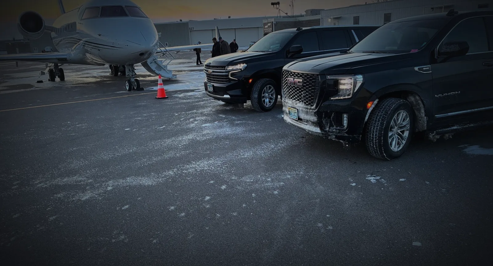 Two black SUVs staged beside a private jet at sunrise on a winter ramp at a Minneapolis FBO