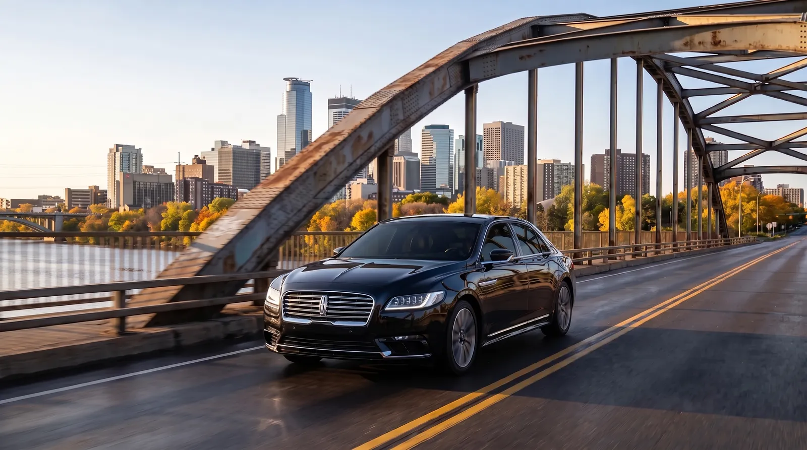 Black Lincoln Continental sedan crossing a Mississippi River bridge toward the Minneapolis skyline on an autumn afternoon